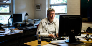 En mand sidder bag en computerskærm på et kirkekontor