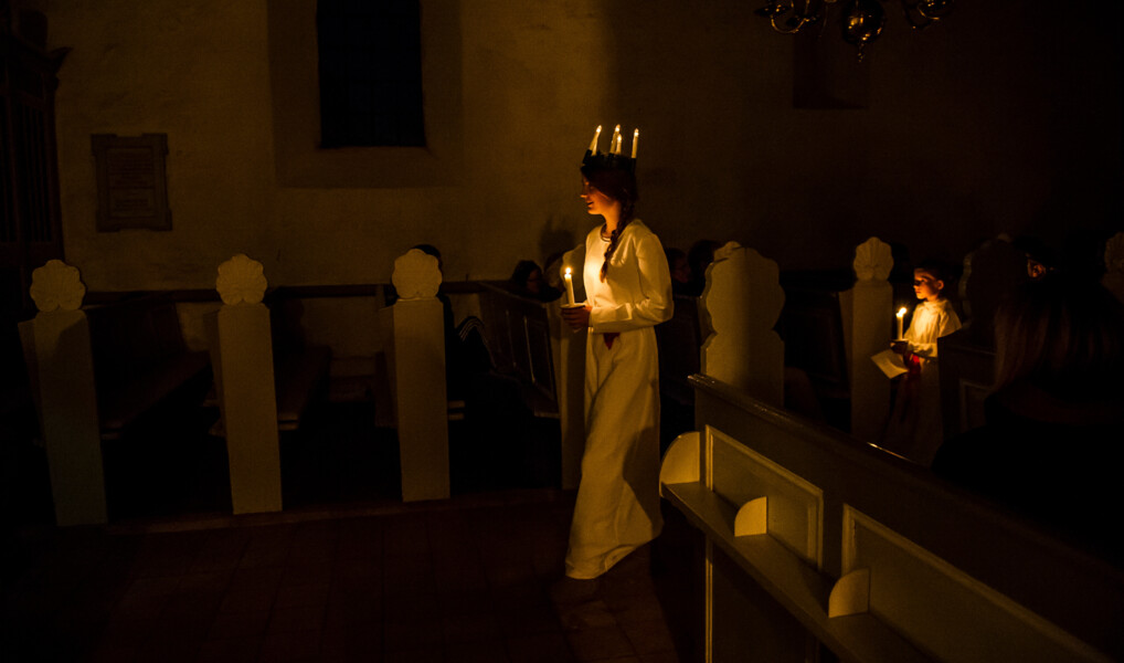 Et luciaoptog lyser op i en mørklagt kirke